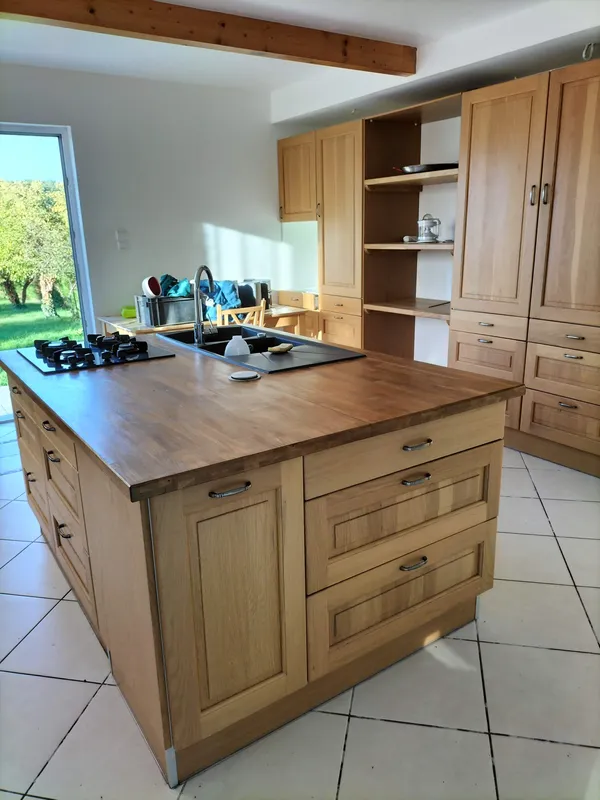 La cuisine avant le projet : îlot et meubles en chêne rustique, évier noir, carrelage beige