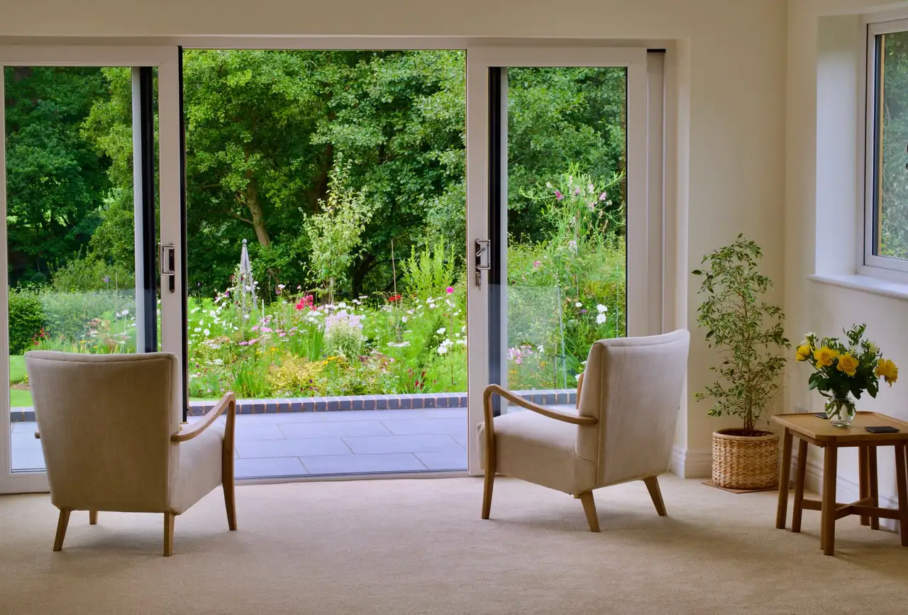 Deux fauteuils en lin face à une baie ouverte sur un jardin fleuri, lumière douce